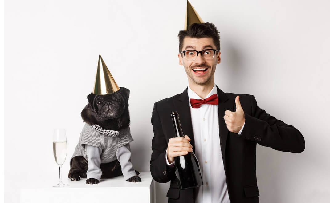 Small black dog wearing a party hat and standing near a happy man celebrating